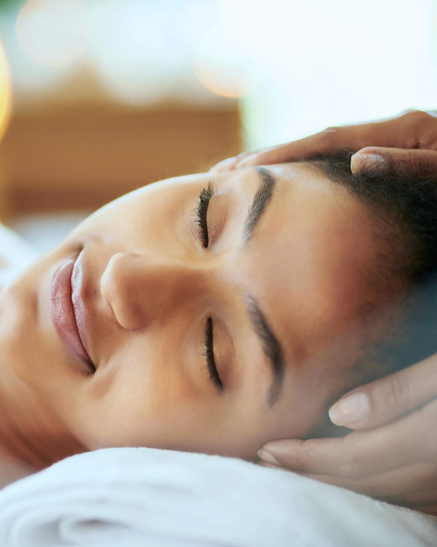Smiling woman with eyes closed, enjoying a head massage.