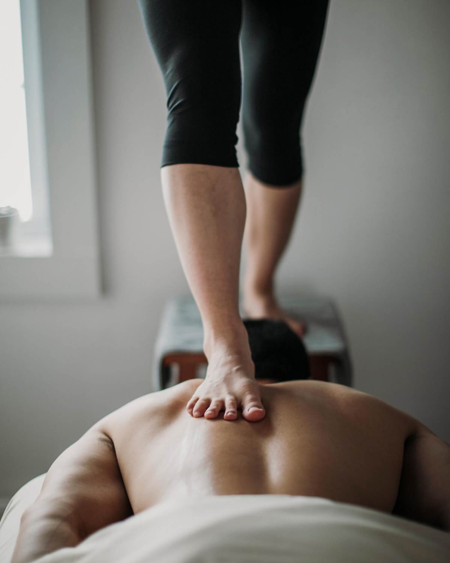 Man receiving deep massage therapy using foot pressure on back.