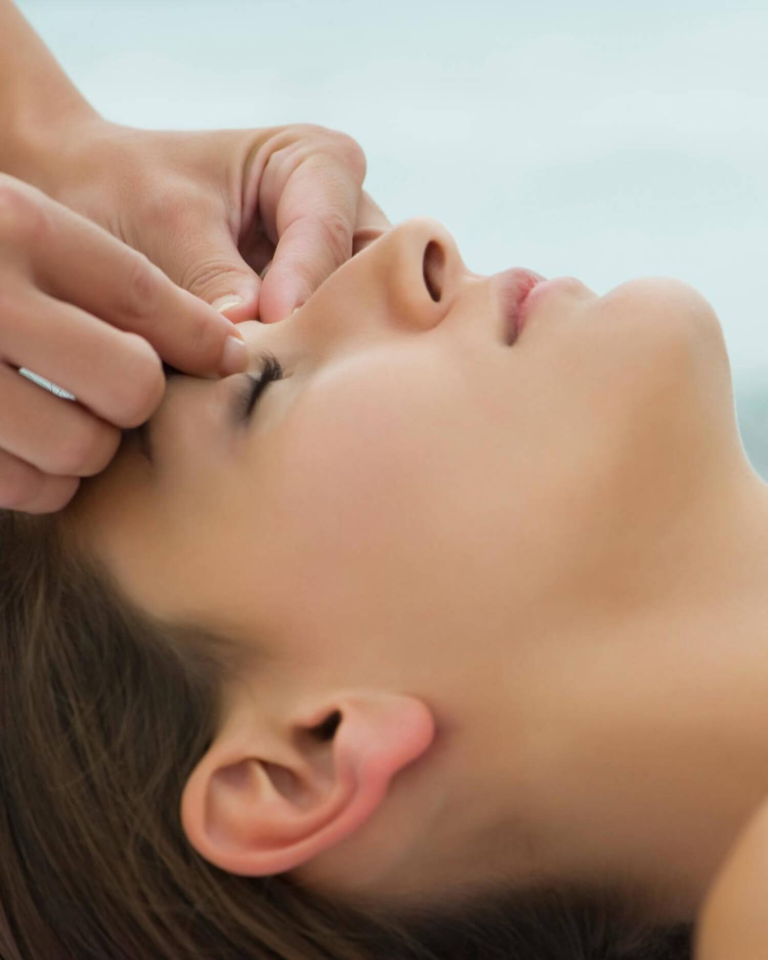 A massage therapist applying pressure to an acupoint near the forehead.